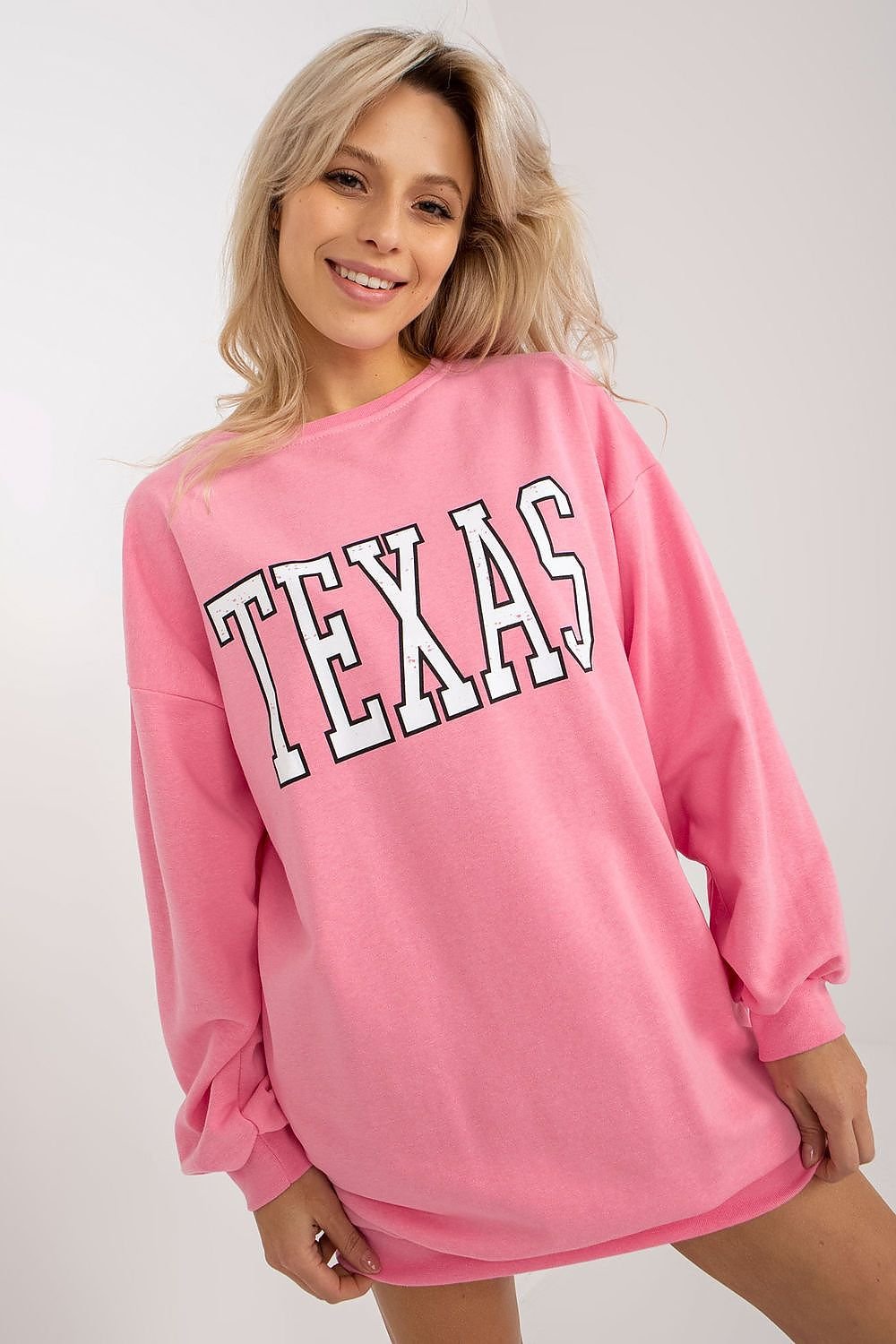 Woman wearing a pink sweatshirt with 'TEXAS' printed on it against a white background