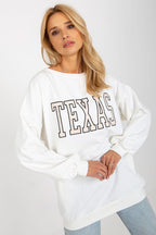 Woman wearing a white sweatshirt with 'TEXAS' printed on it against a plain background