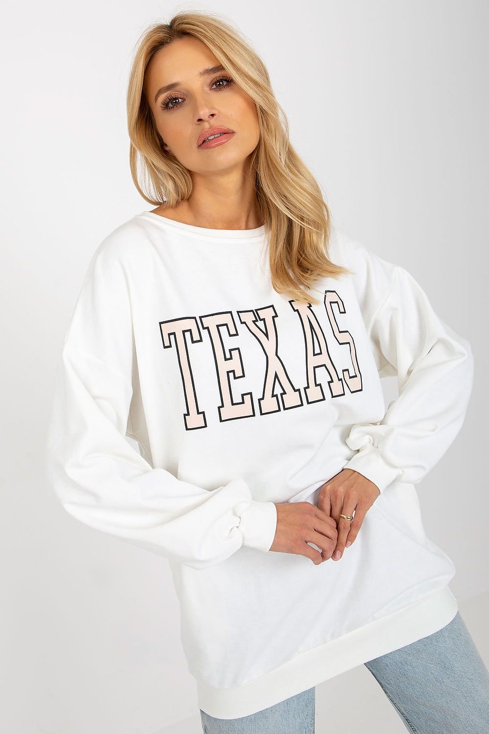 Woman wearing a white sweatshirt with 'TEXAS' printed on it against a plain background