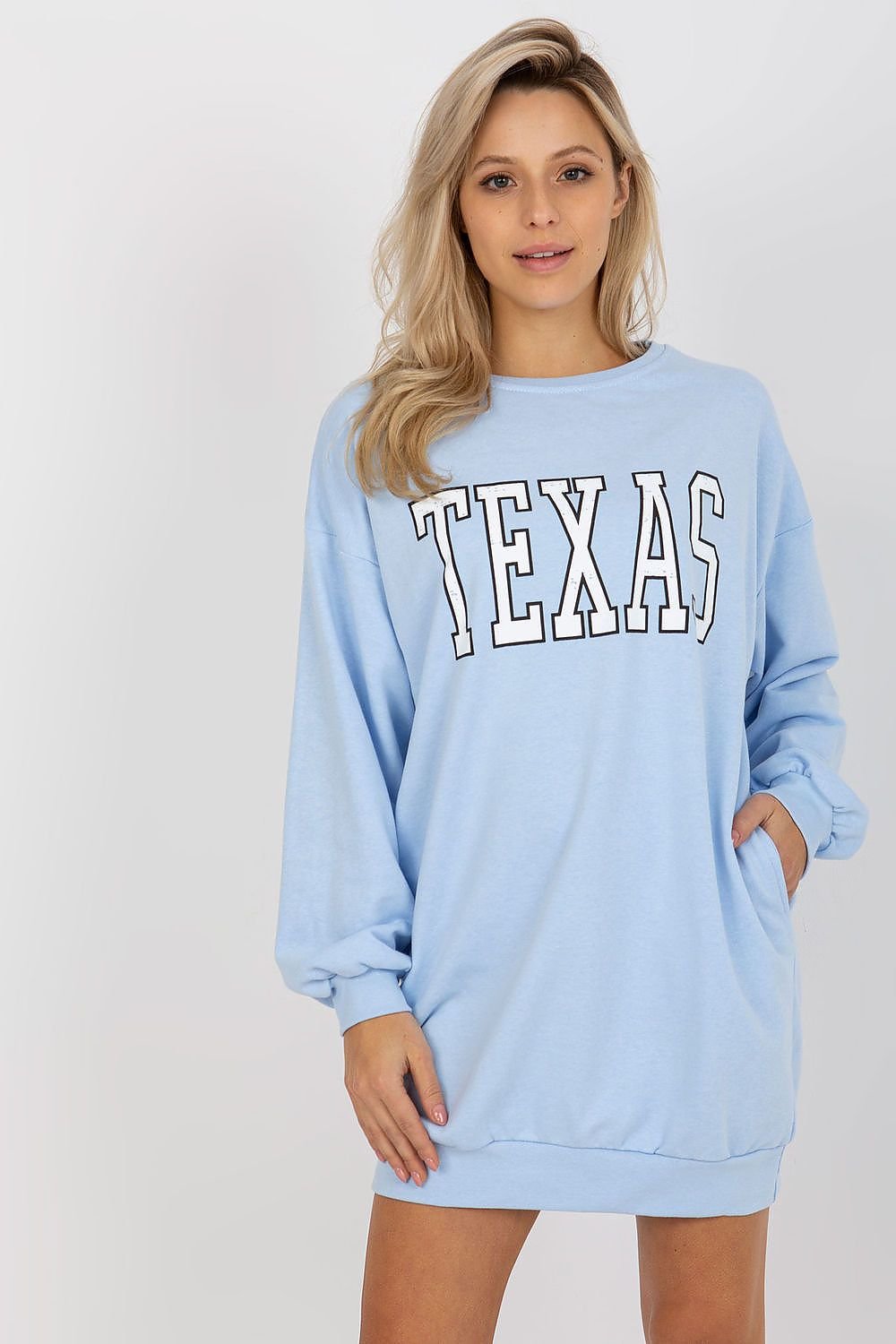 Woman wearing a light blue sweatshirt with 'TEXAS' printed on it against a white background