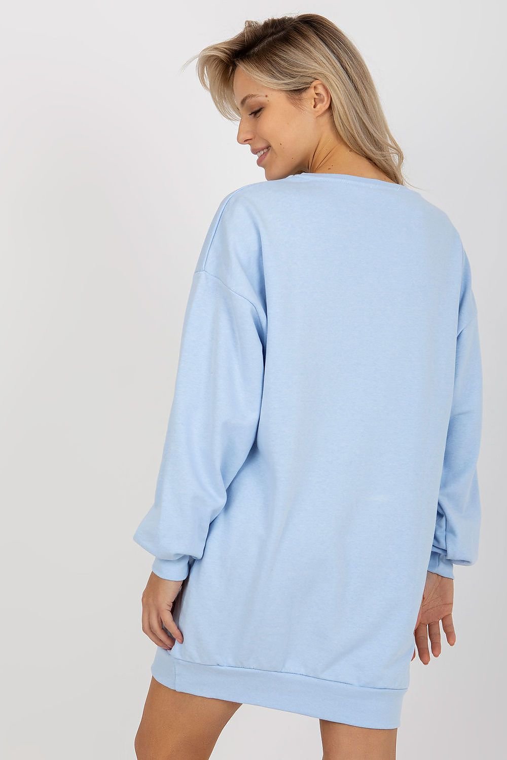 Woman wearing a light blue sweatshirt dress against a white background