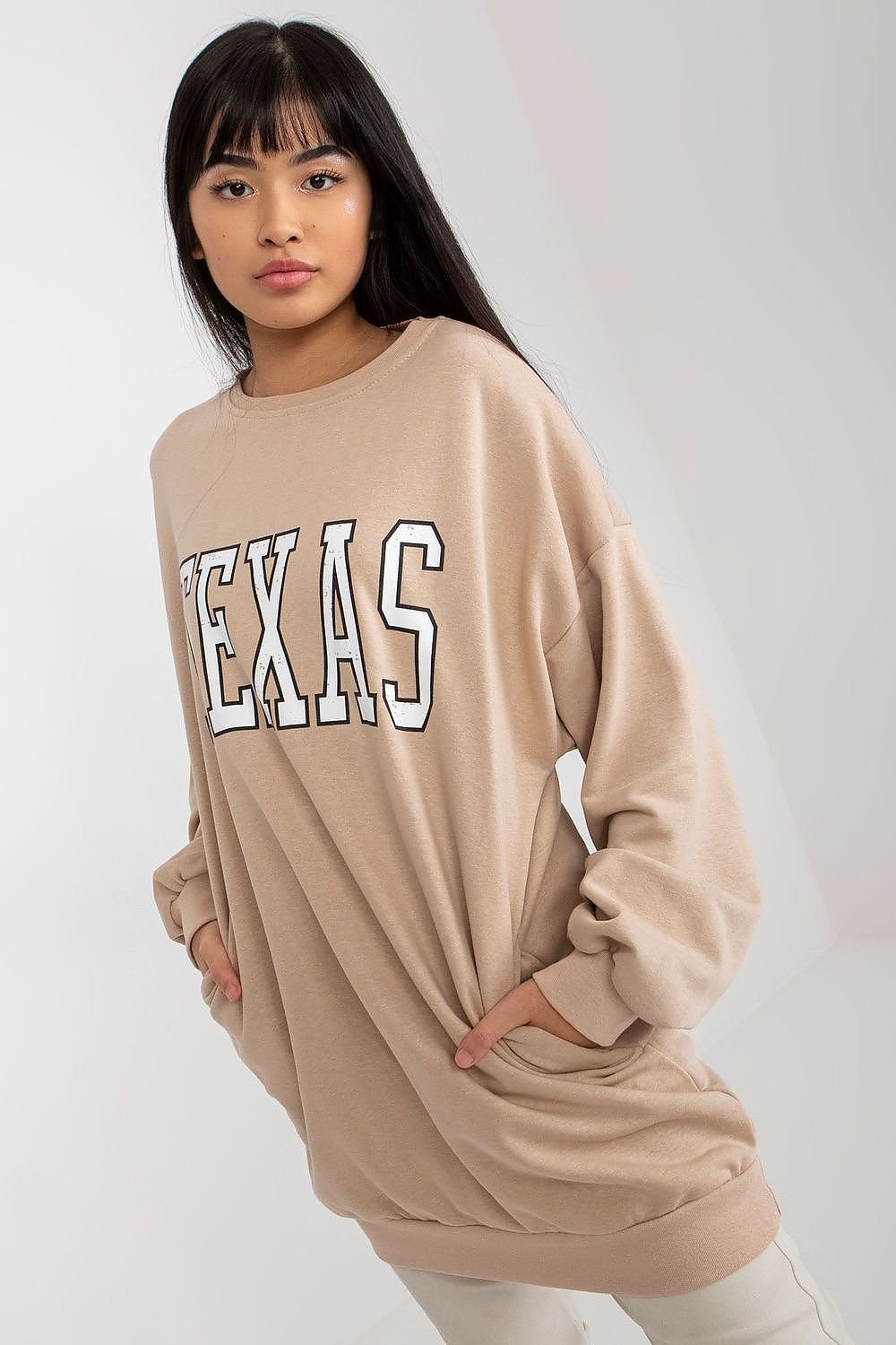 Woman wearing a beige sweatshirt with 'TEXAS' printed on it against a white background