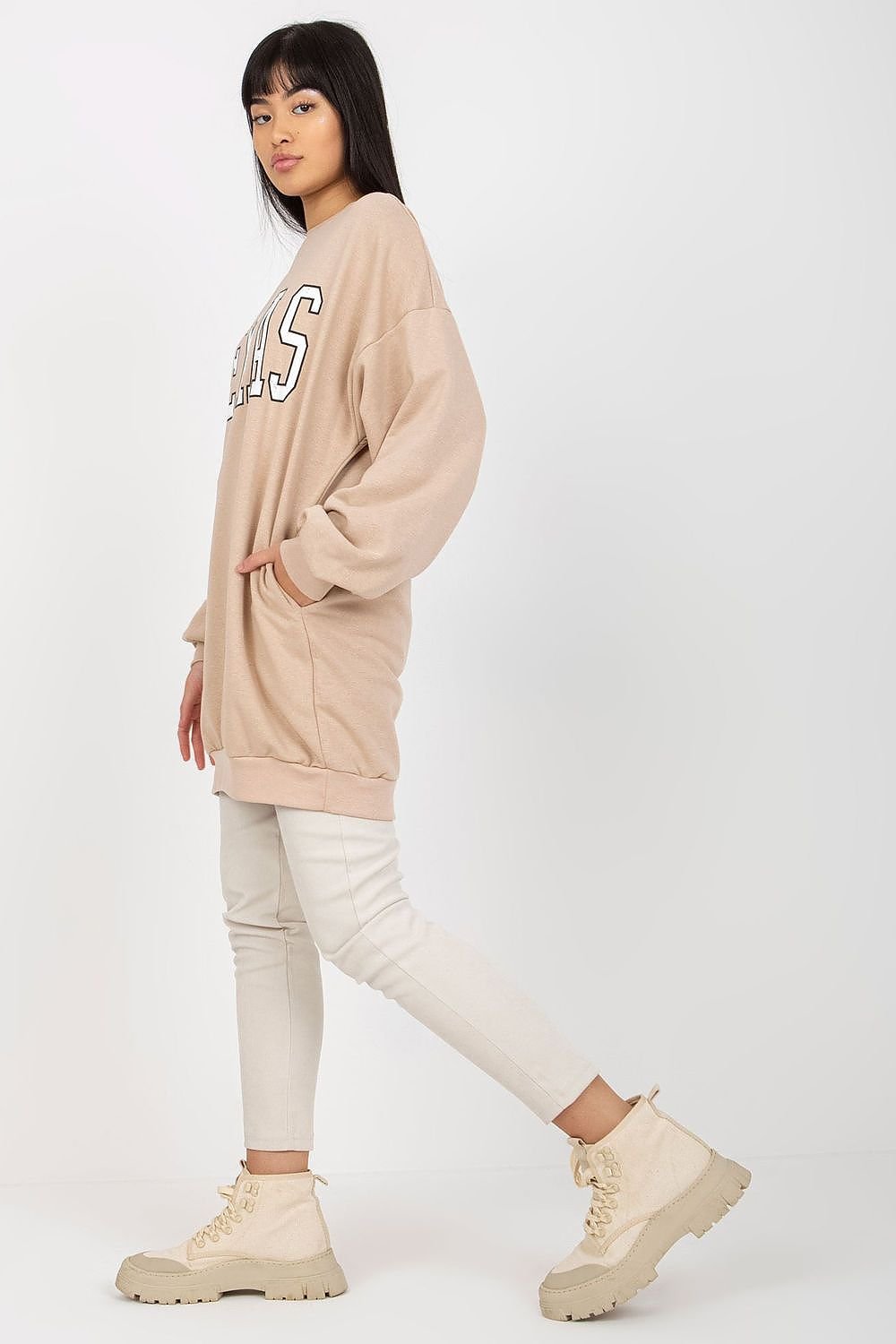 Woman wearing a beige oversized sweatshirt and pants with beige boots on a white background