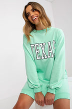 Woman wearing a light green 'TEXAS' sweatshirt and shorts on a white background