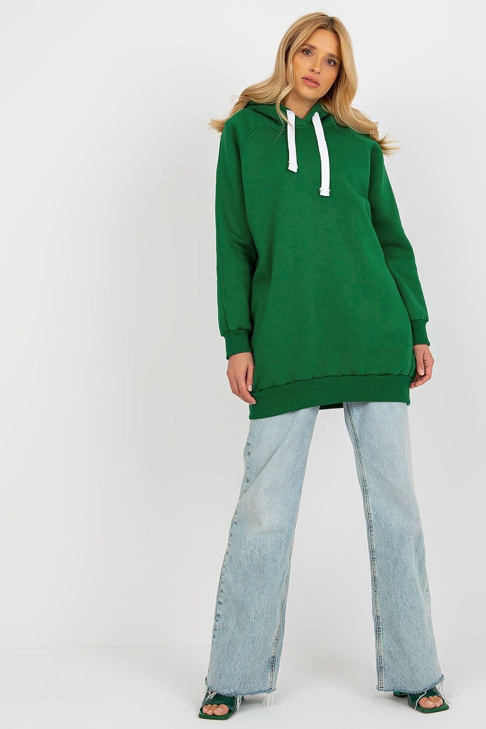 Woman wearing a green hoodie and light blue jeans on a white background