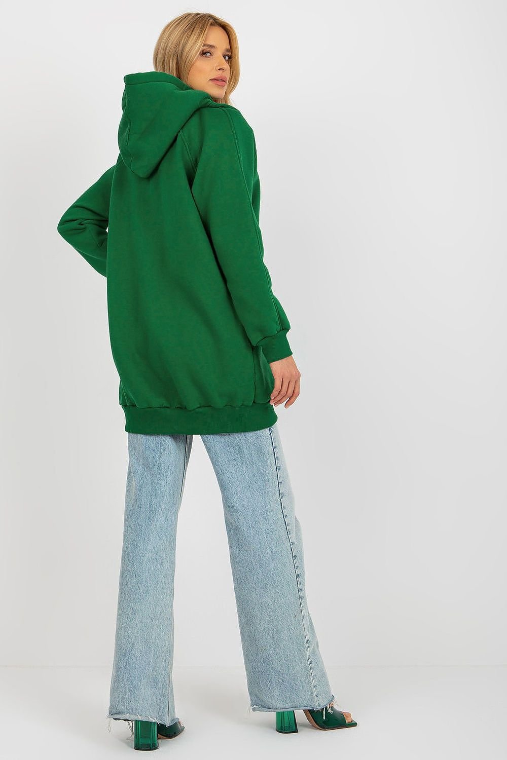 Person wearing a green hoodie and light blue jeans on a white background