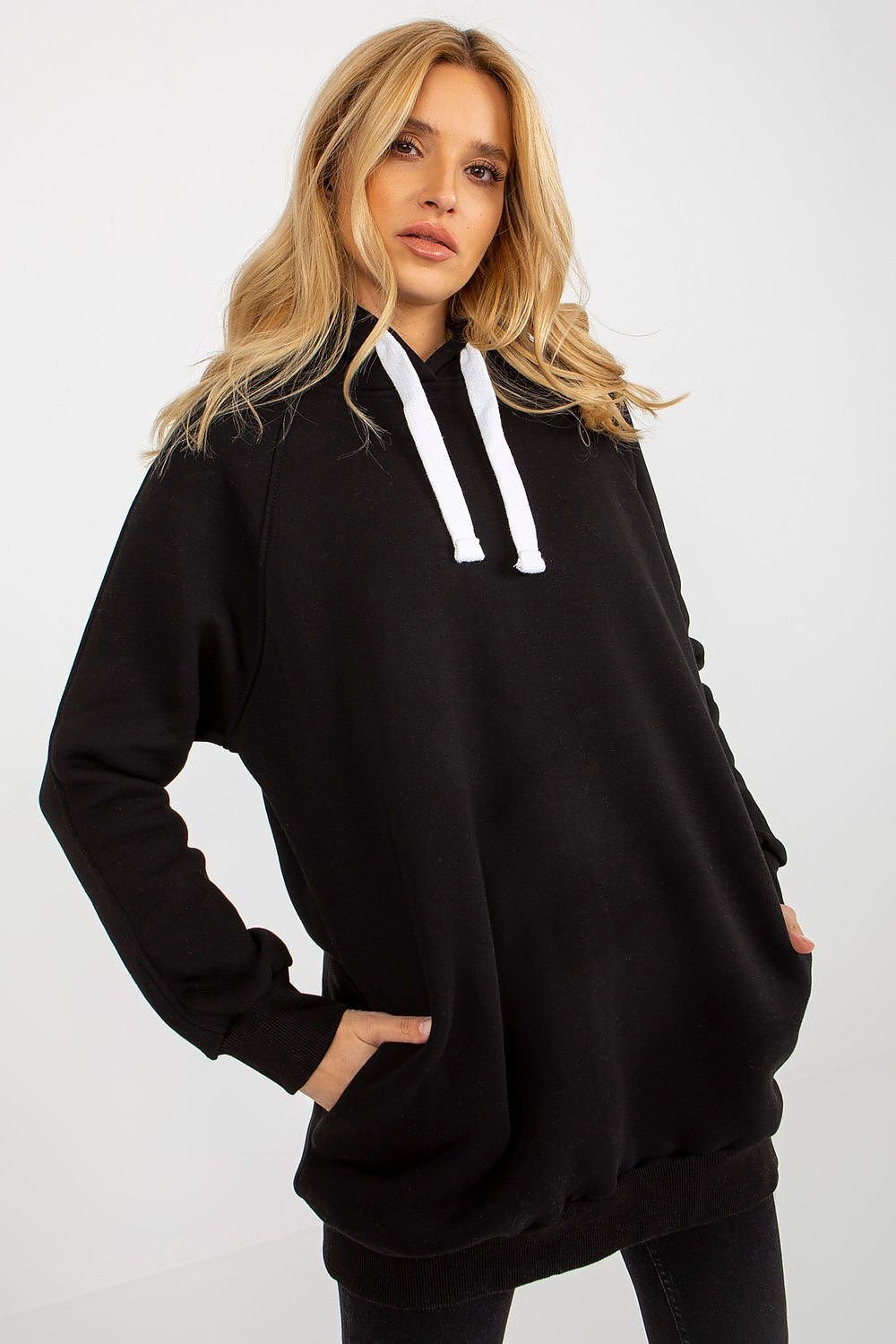 Woman wearing a black hoodie with white drawstrings on a plain background