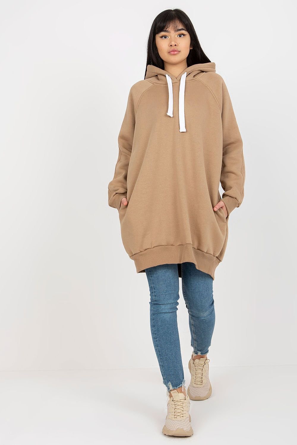Person wearing a beige hoodie and blue jeans on a white background