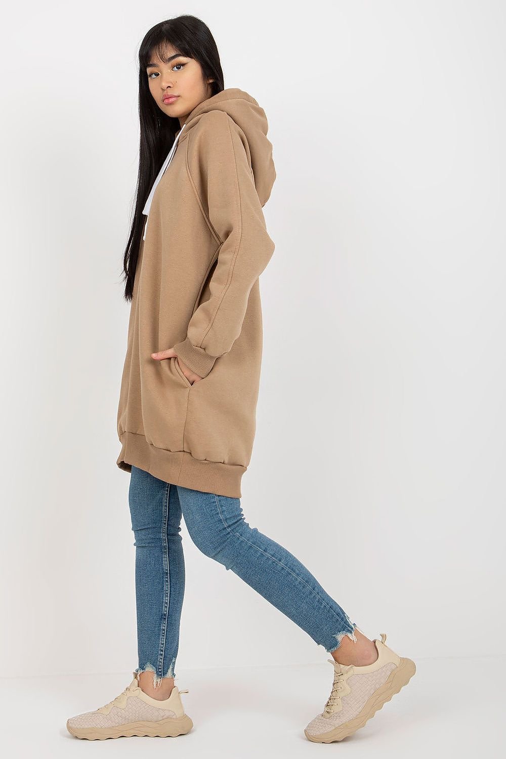 Person wearing a beige hoodie and blue jeans on a white background