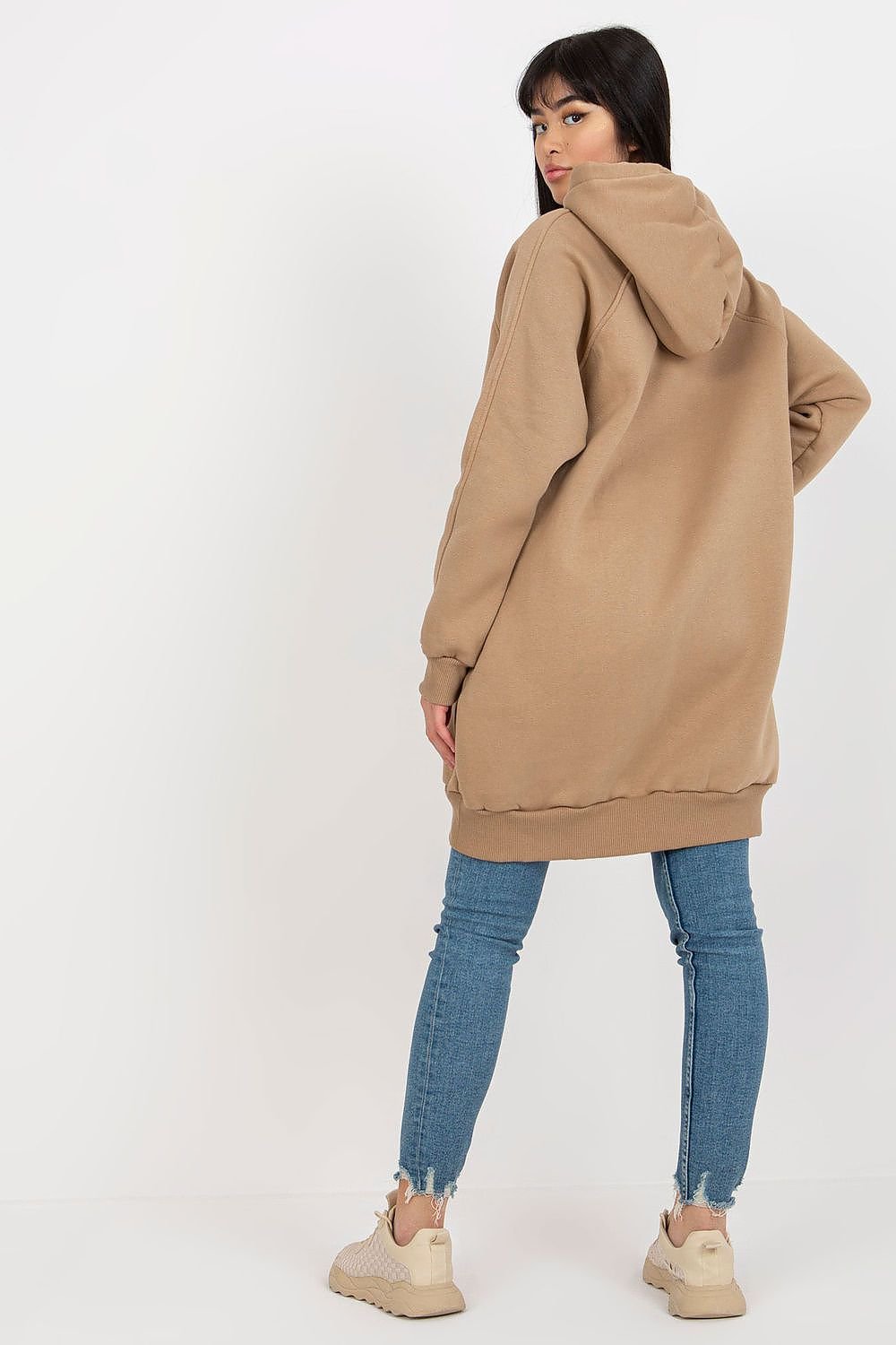 Person wearing a beige hoodie and blue jeans on a white background