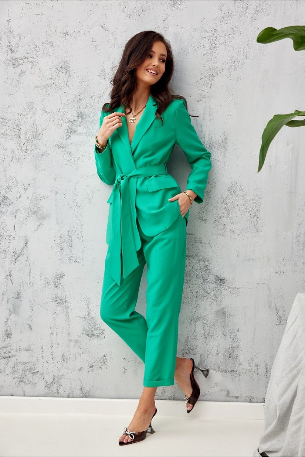 Woman in a green jumpsuit standing against a gray concrete wall.