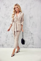 Woman wearing a beige suit with a belt, holding a black handbag against a light gray background
