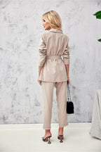 Woman wearing a beige trench coat and pants against a light gray wall.