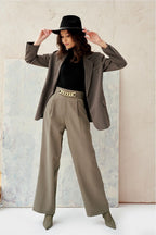 Woman wearing a gray blazer, beige pants, black top, and hat against a light background