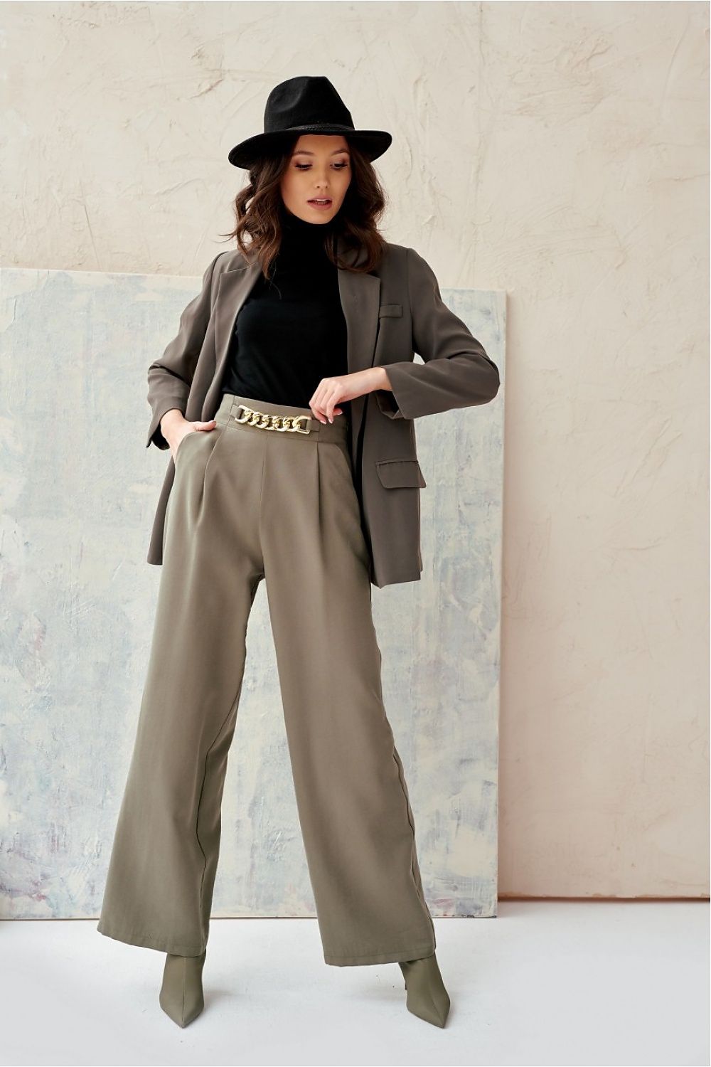 Woman wearing a brown suit with wide-leg pants and a black hat against a neutral background