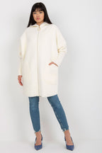 Woman wearing a cream coat and blue jeans on a white background