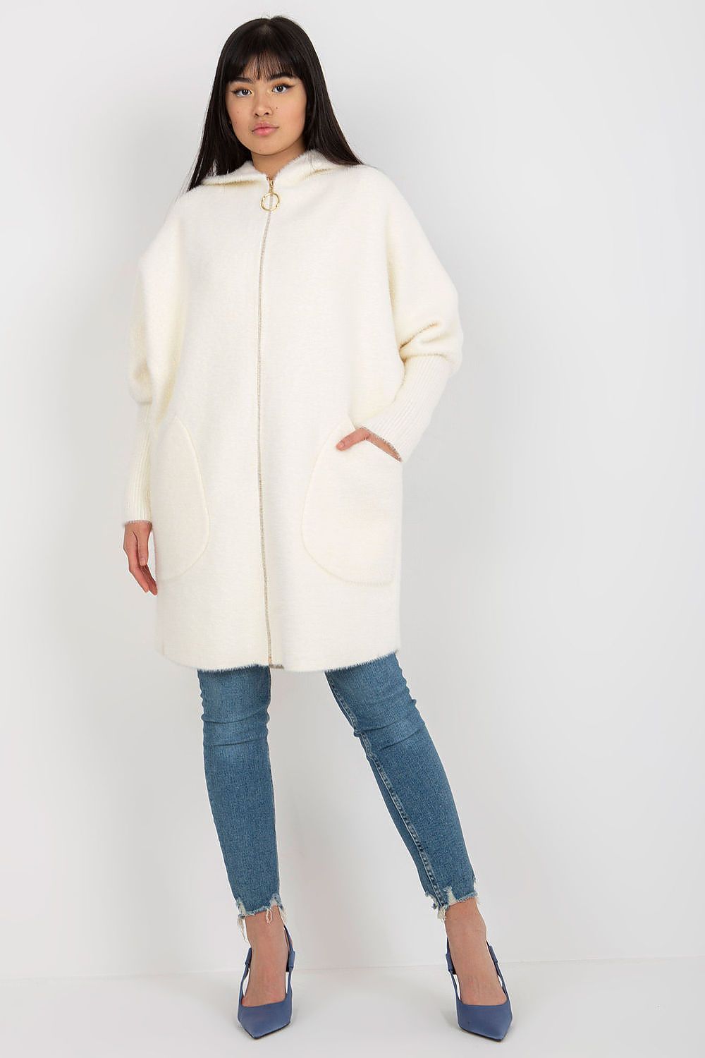 Woman wearing a cream coat and blue jeans on a white background