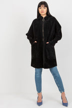 Person wearing a black hooded coat and blue jeans on a white background