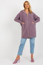 Woman wearing a long, hooded purple jacket and blue jeans on a white background