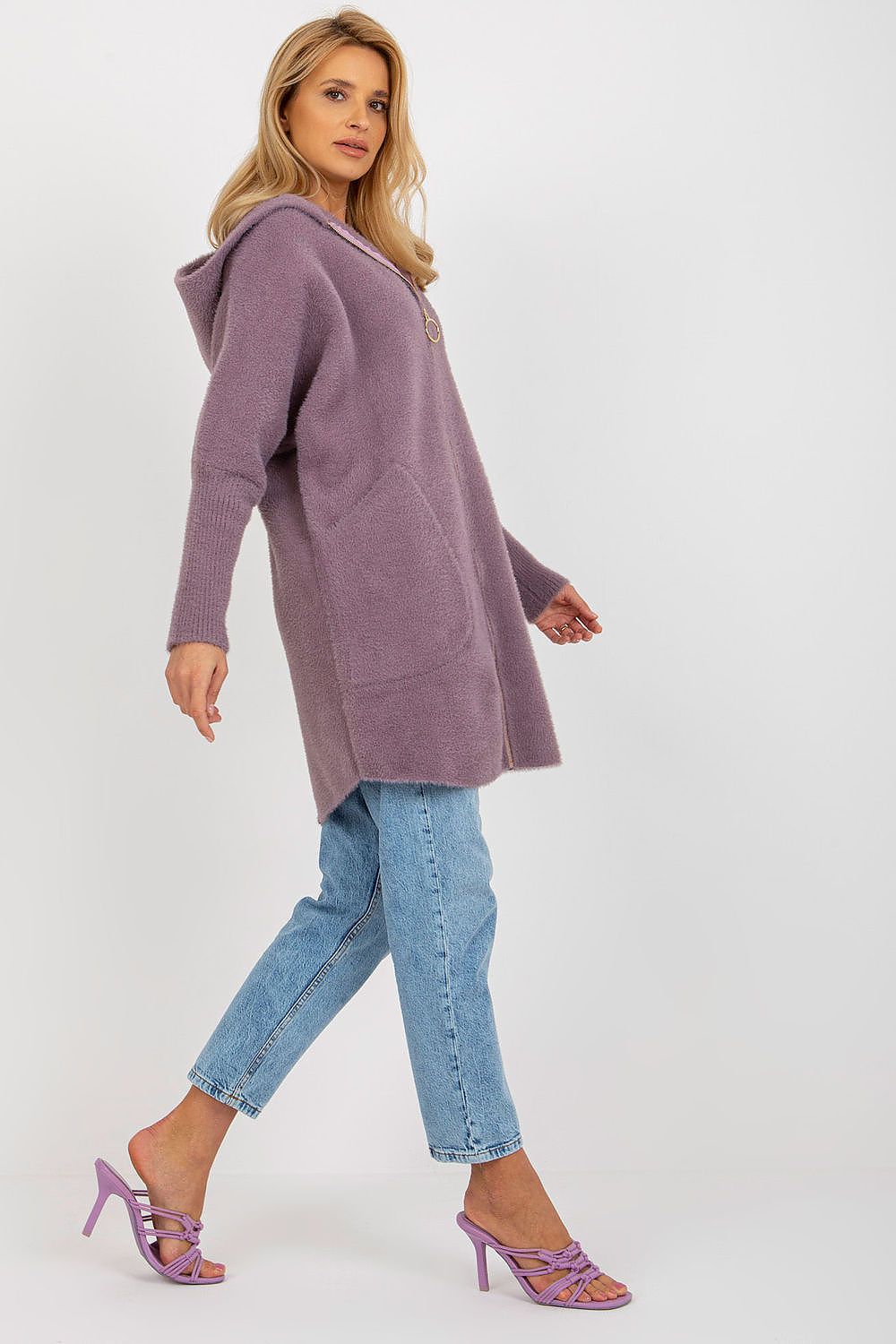 Woman wearing a long, light purple cardigan over a blue top and jeans on a white background