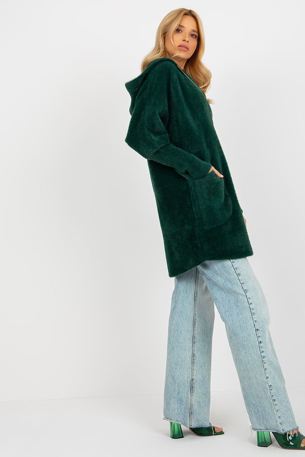 Woman wearing a green cardigan and light blue jeans on a white background
