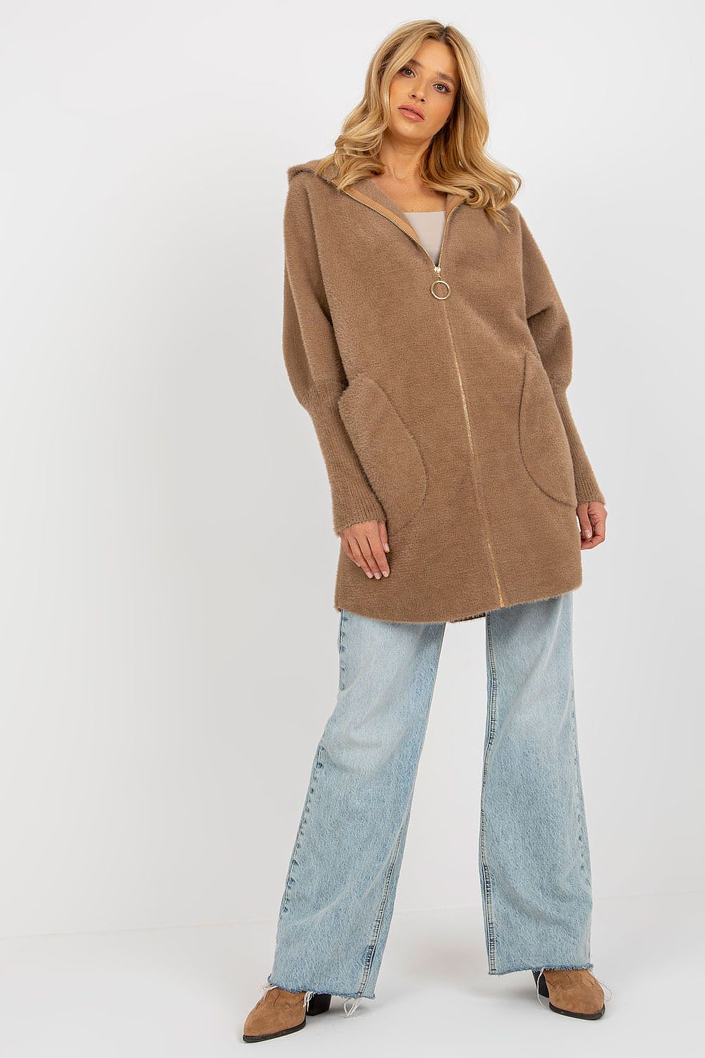 Woman wearing a brown coat and light blue jeans on a white background
