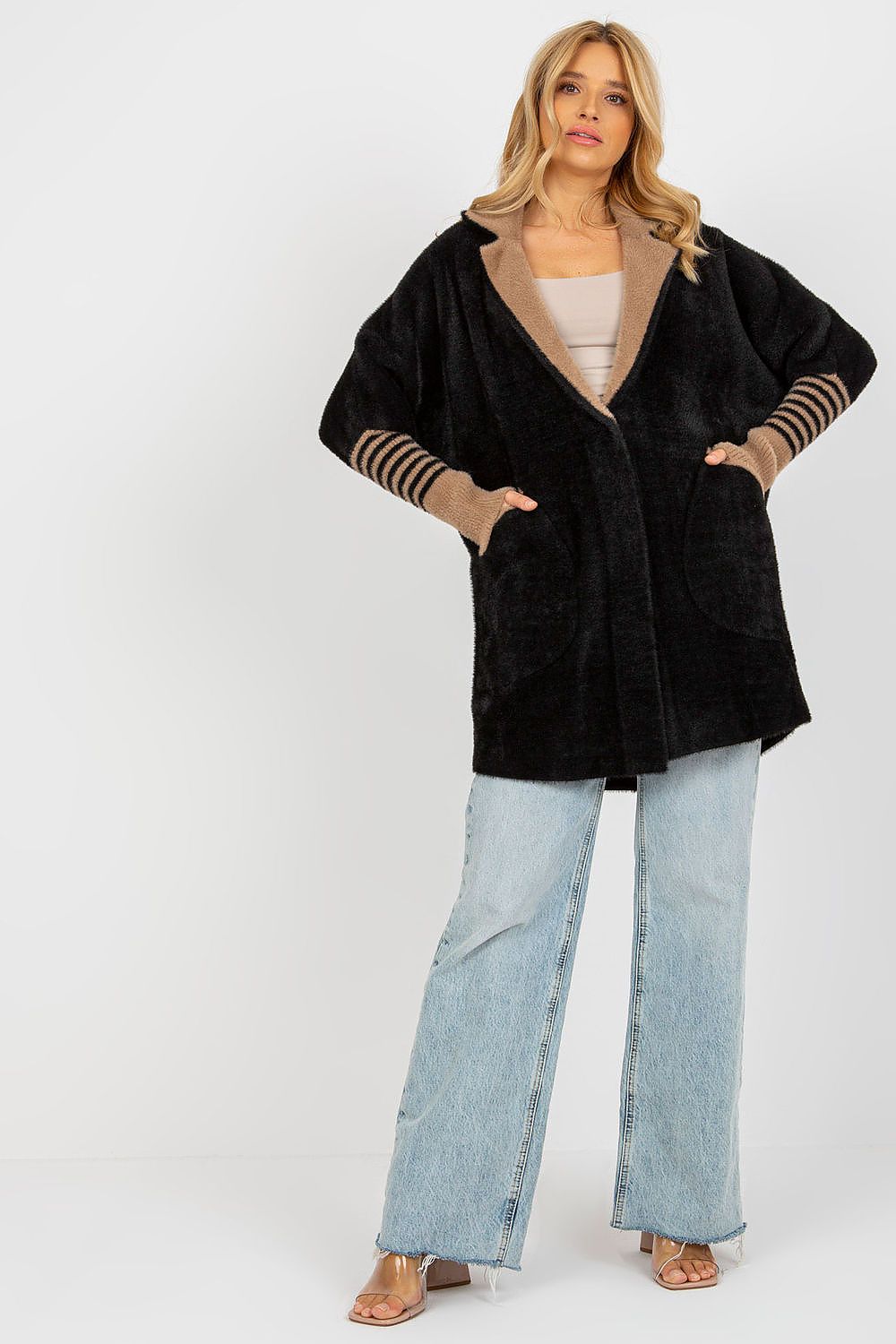 Woman wearing a black cardigan with striped sleeves and light blue jeans on a white background