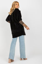 Woman wearing a black coat with striped cuffs and light blue jeans on a white background