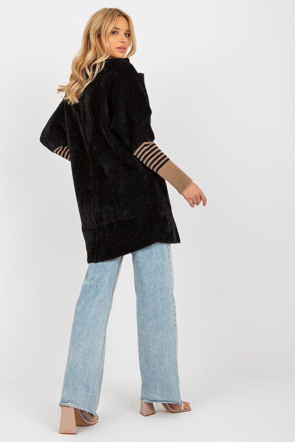 Woman wearing a black coat with striped cuffs and light blue jeans on a white background