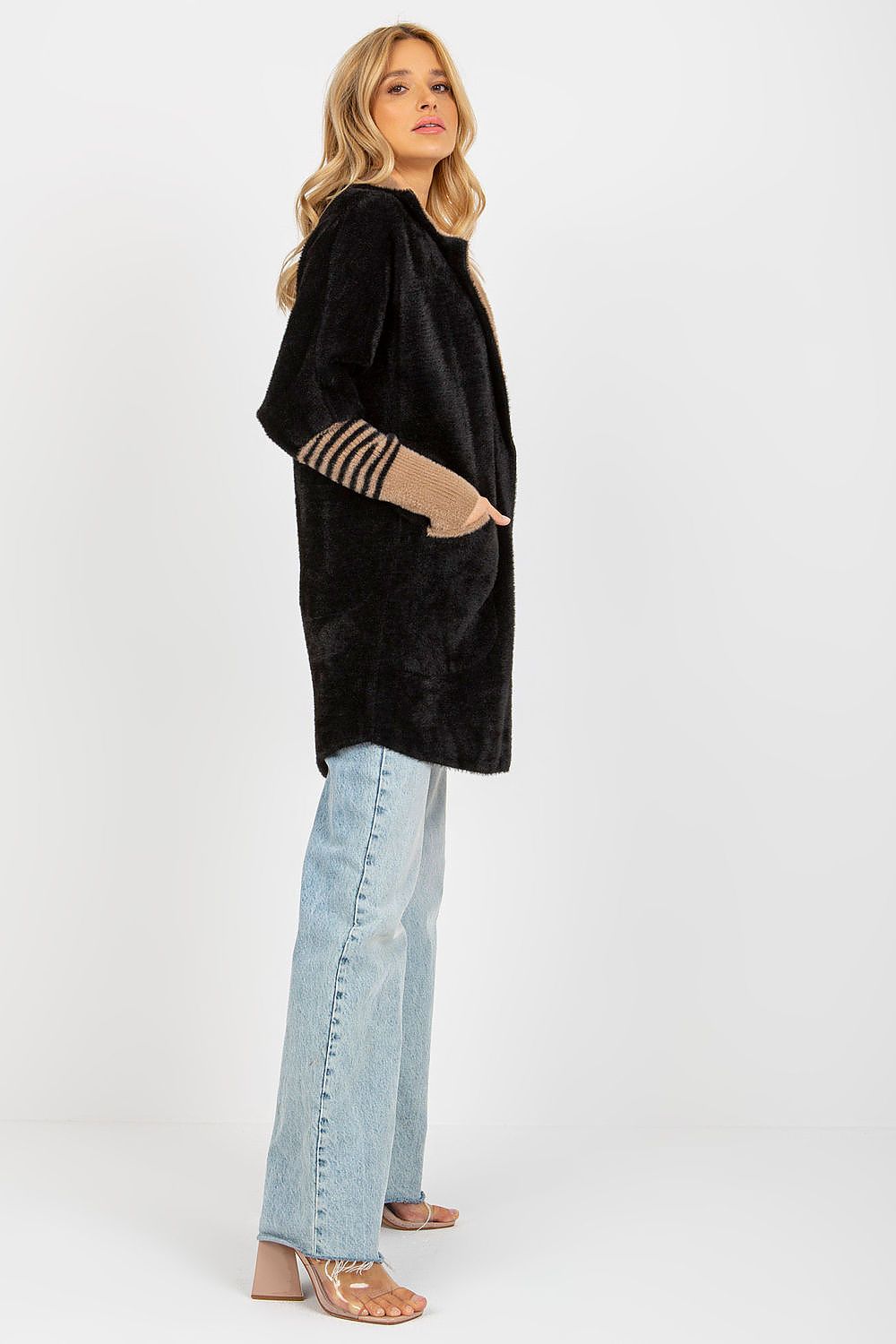 Woman wearing a black oversized sweater with striped cuffs and light blue jeans on a white background