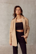 Woman wearing a beige coat over a black outfit against a plain background