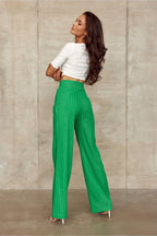 Woman wearing a white top and green pinstripe pants against a beige wall.
