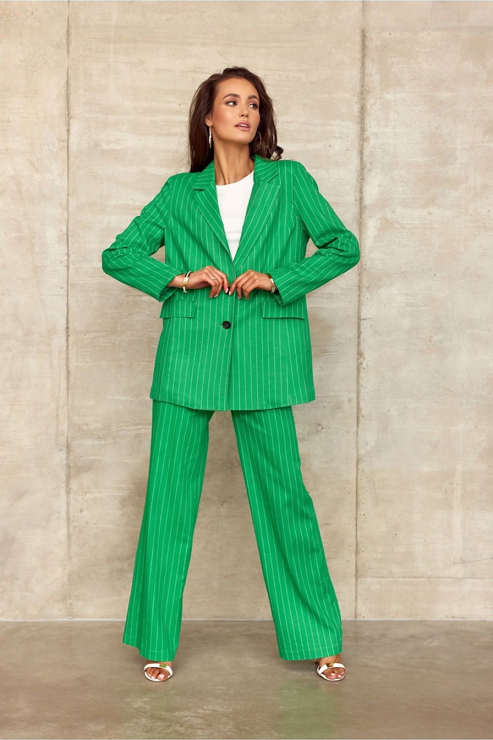 Woman wearing a green pinstripe suit against a beige wall.