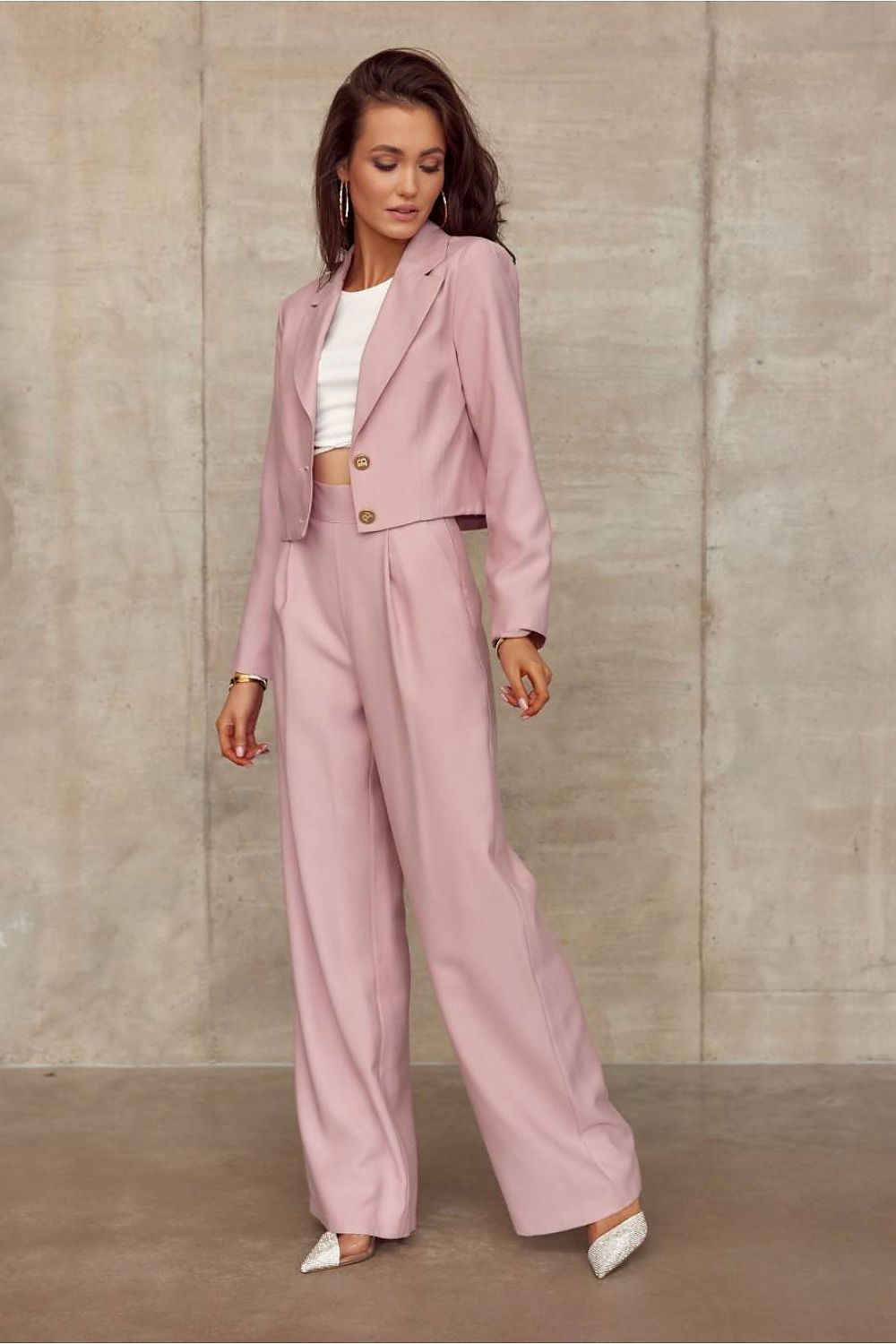Woman wearing a pink suit with a white top against a beige wall.