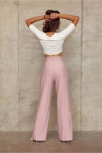Person wearing a white long-sleeve top and pink high-waisted pants against a beige wall.