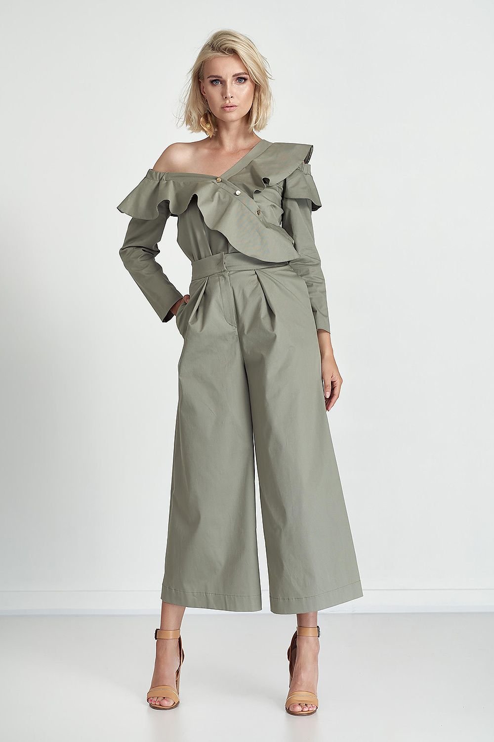Woman wearing a green off-shoulder top and wide-leg pants on a white background