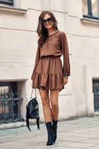 Woman wearing a brown dress with black boots and sunglasses, standing on a street.