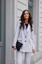 Woman in a striped suit standing against a light-colored wall.