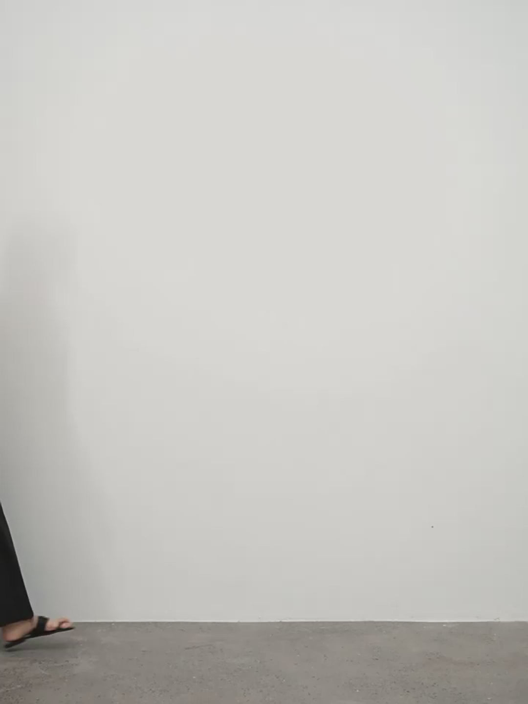 Person wearing black sandals standing on a gray floor against a white wall