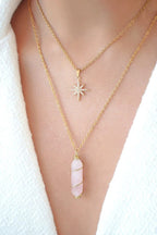 Two gold necklaces with pendants on a person wearing a white garment.