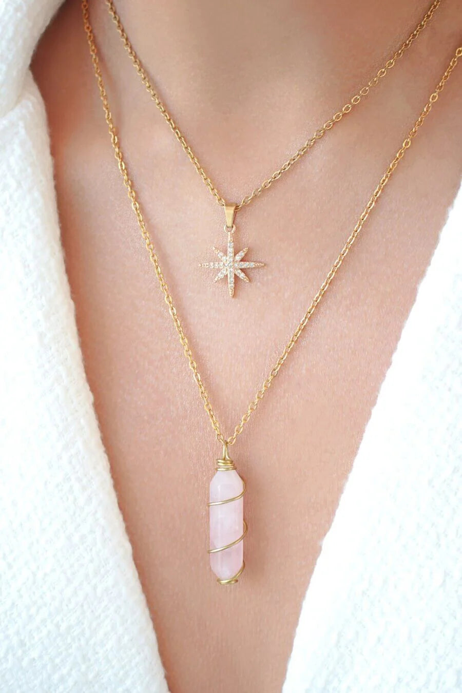Two gold necklaces with pendants on a person wearing a white garment.