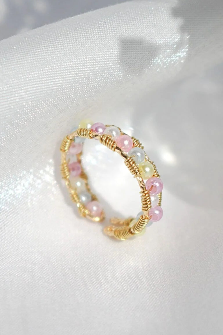 Gold and pink beaded ring on a white fabric background