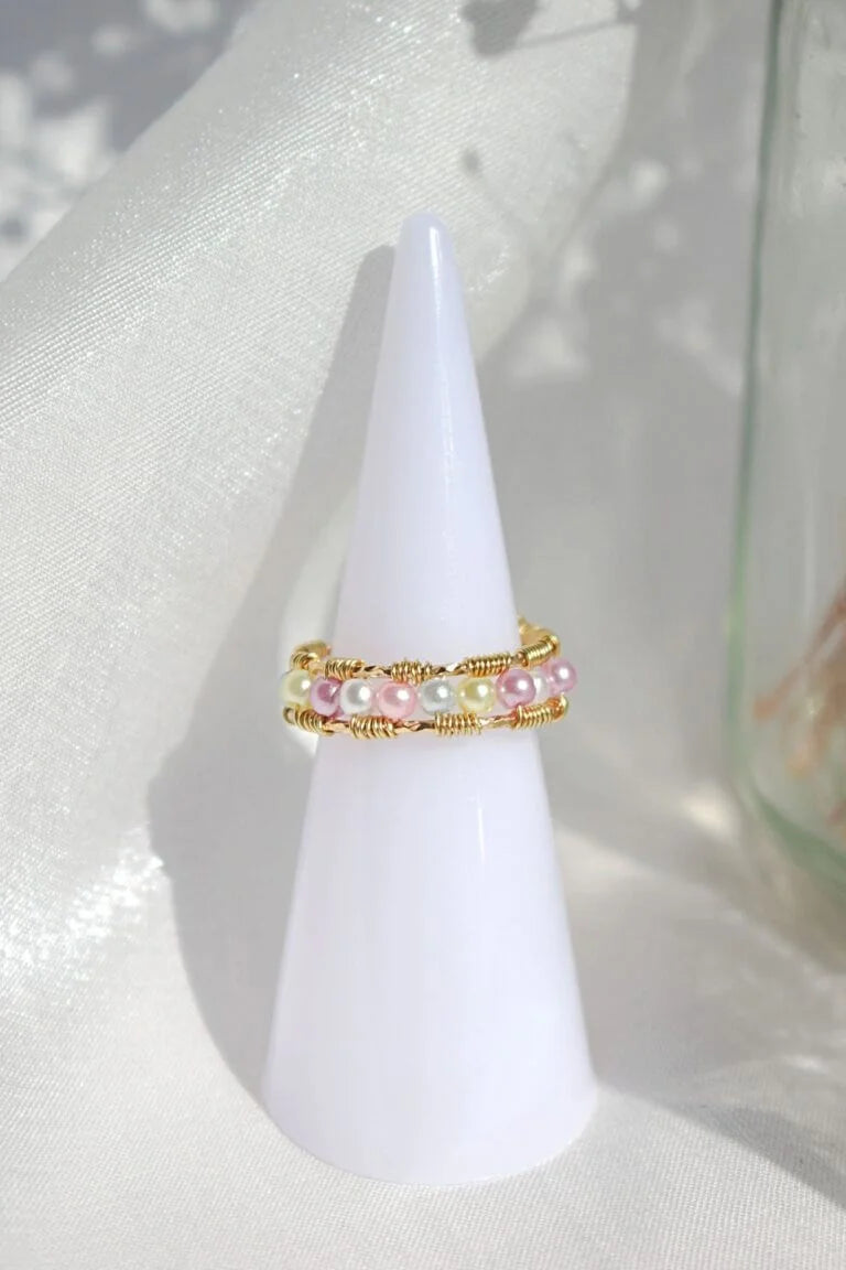 Two pearl rings on a white cone-shaped stand with a light background