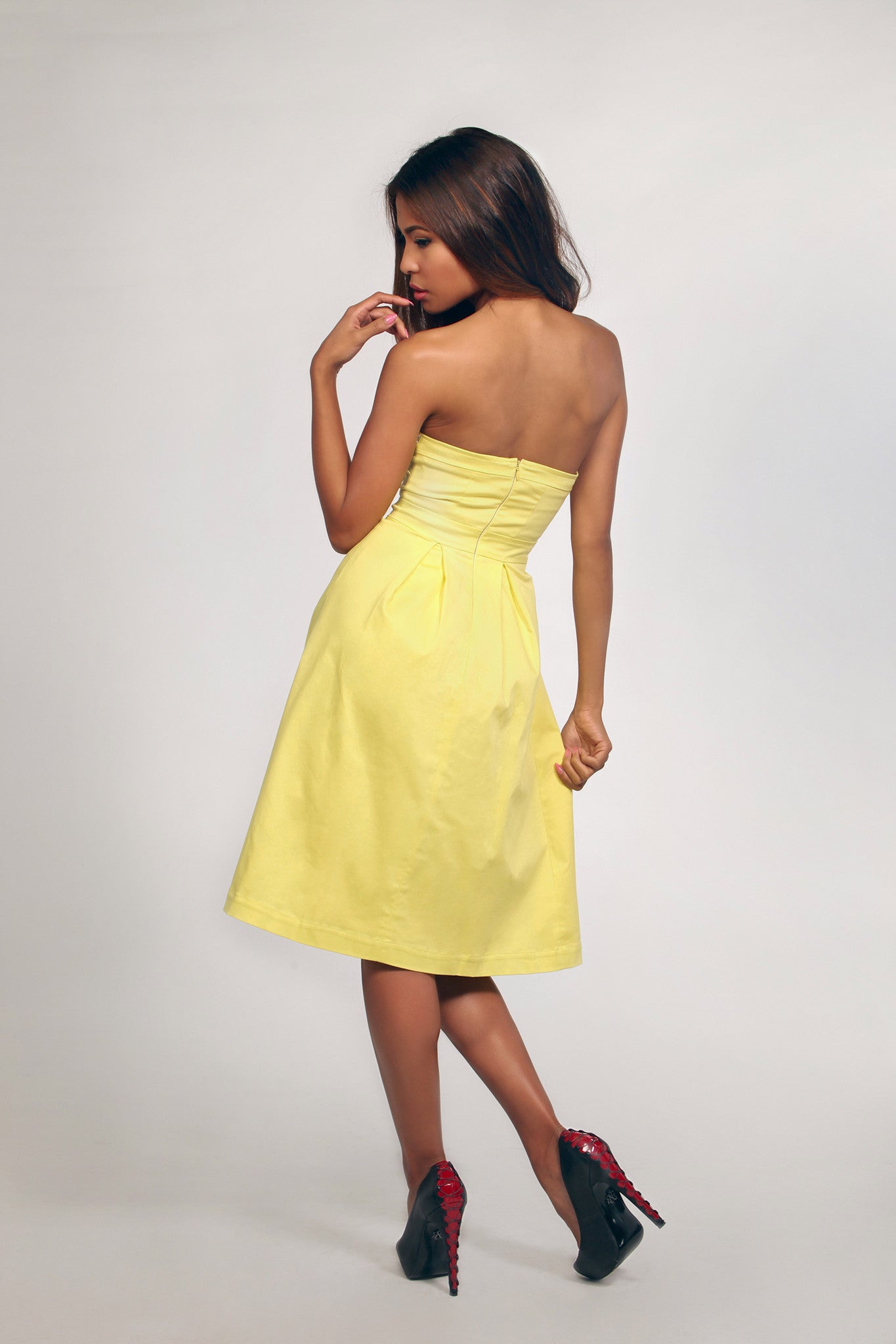 Woman wearing a yellow strapless dress on a plain background